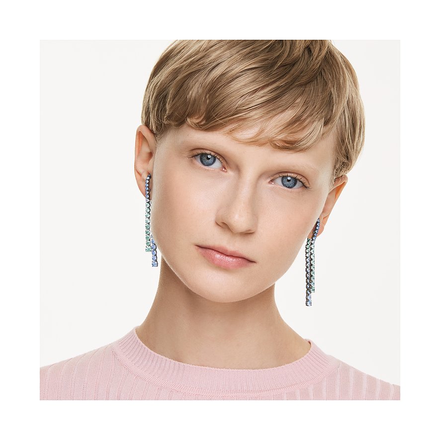 Een model draagt lange, hangende metalen Swarovski oorbellen met kleurrijke Swarovski-kristallen in blauw- en groentinten.