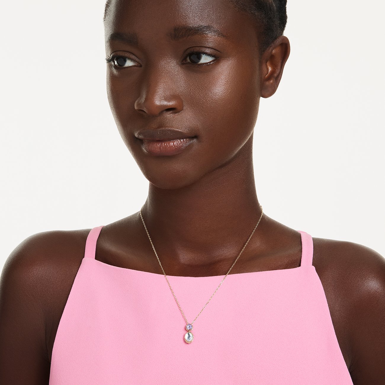 Ein Model trägt eine Goldkette mit einem länglichen Anhänger in rosa und hellblauem Swarovski-Kristall.