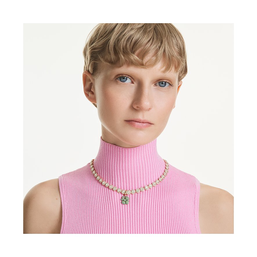 Model draagt een goudkleurige Swarovski metalen ketting met individuele heldere kristallen en een groene klaverhanger.