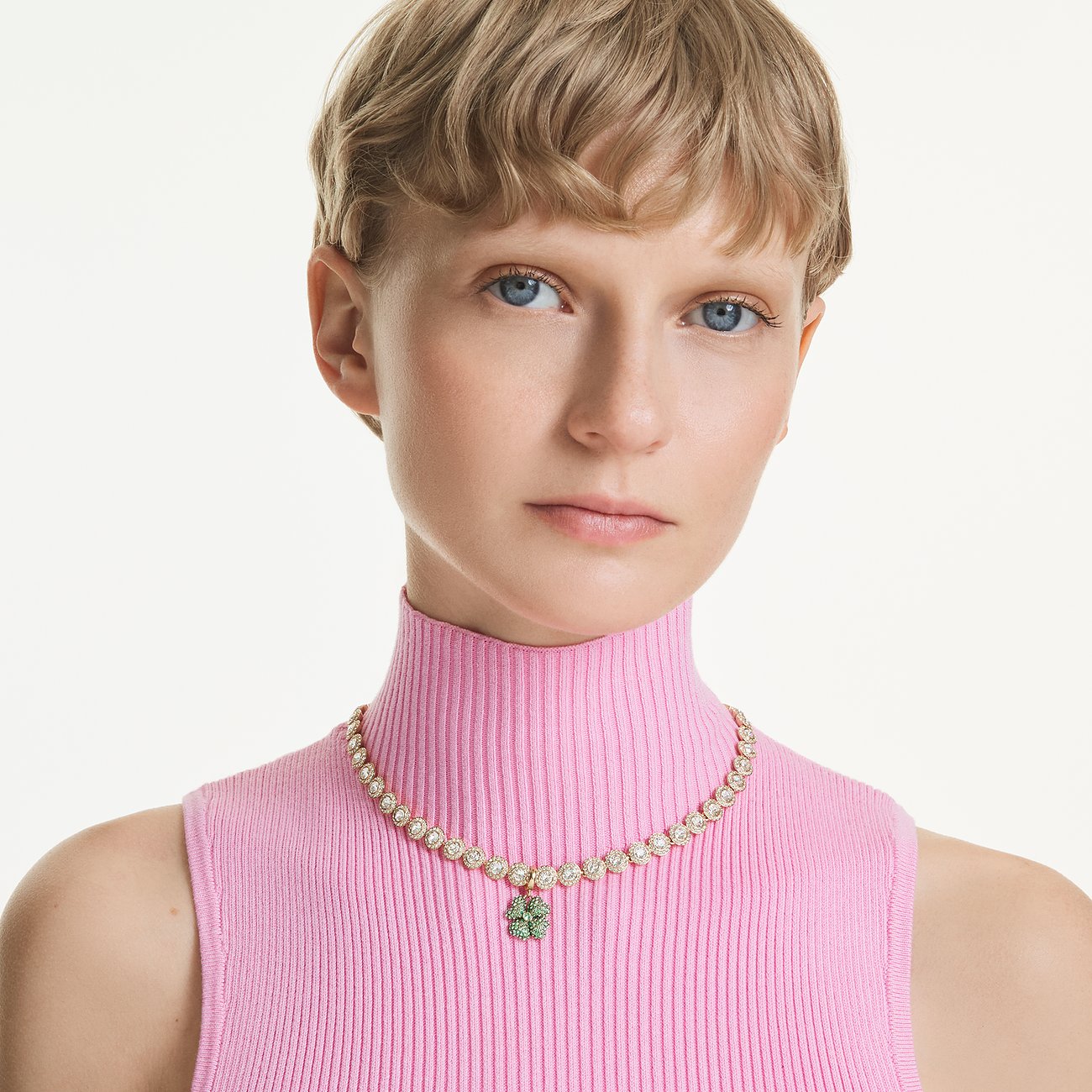 Model draagt een goudkleurige Swarovski metalen ketting met individuele heldere kristallen en een groene klaverhanger.
