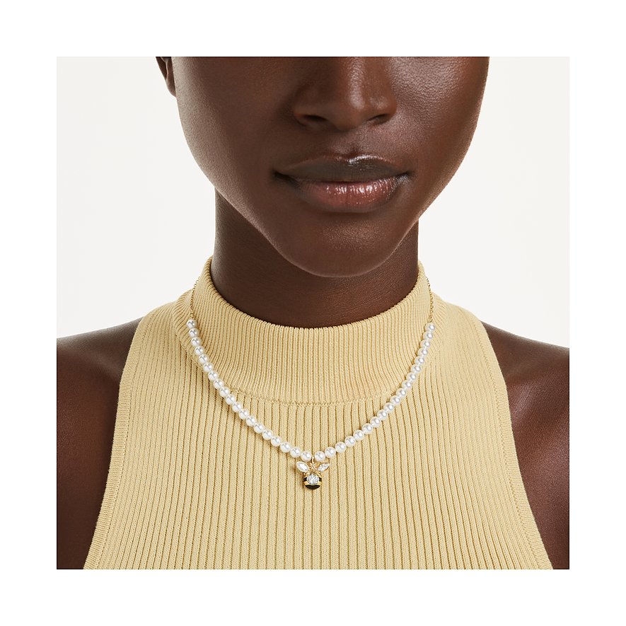 Nahaufnahme einer Person, die eine Halskette aus weißen Perlen und einem funkelnden Swarovski-Kristall-Anhänger trägt.