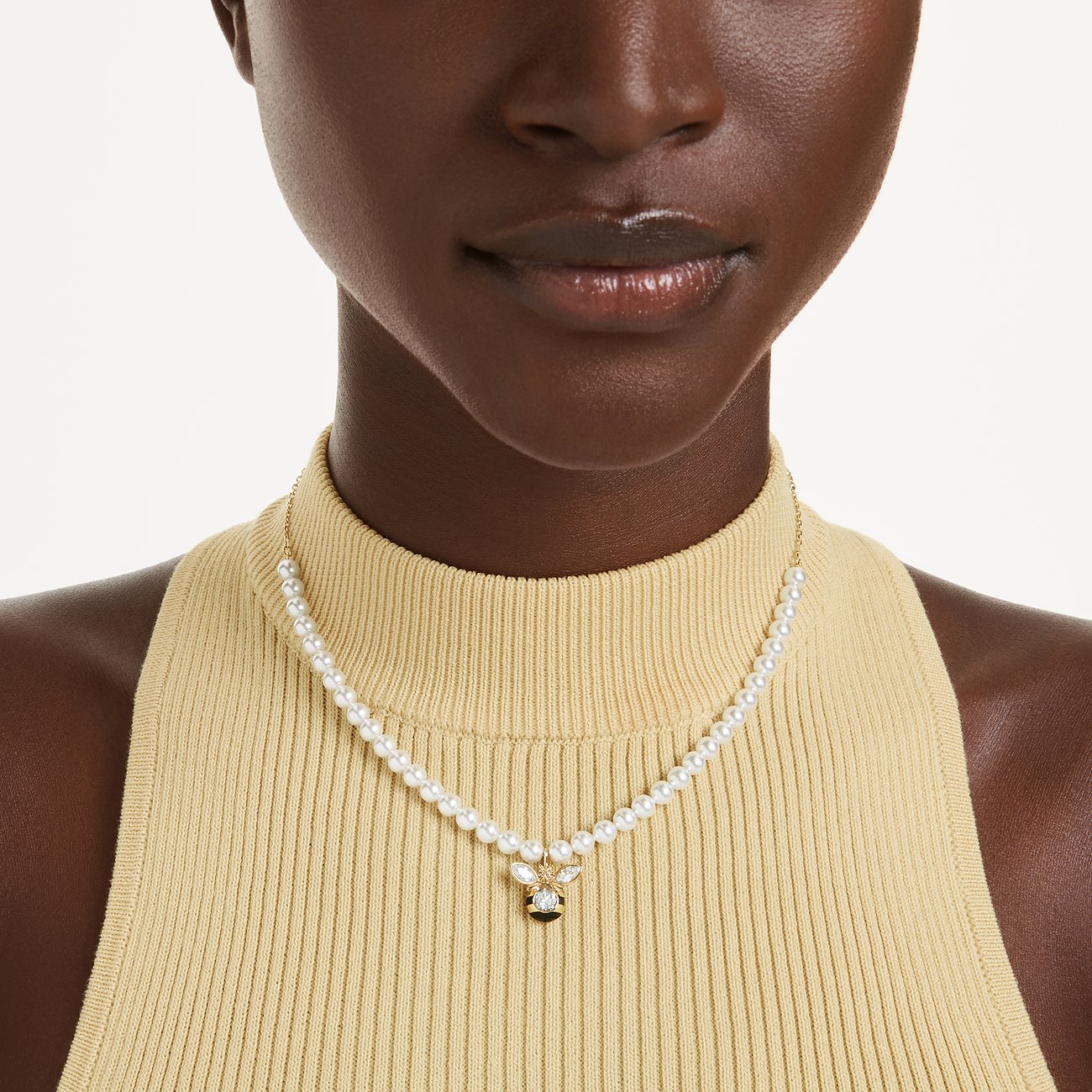 Nahaufnahme einer Person, die eine Halskette aus weißen Perlen und einem funkelnden Swarovski-Kristall-Anhänger trägt.