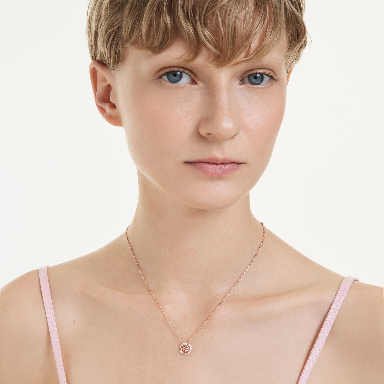 Model trägt eine Swarovski Halskette aus roségoldfarbenem Metall mit einem kleinen, runden Anhänger mit Farbedelsteinen.