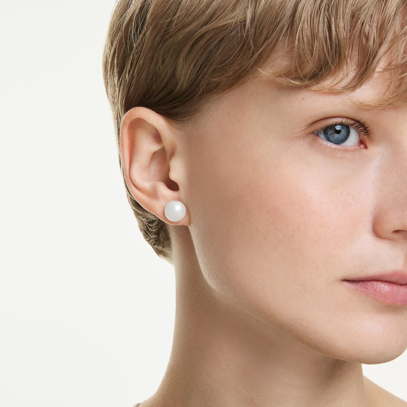 Nahaufnahme einer Person mit einem einzelnen runden, weißen Swarovski Ohrstecker aus Metall an einem Ohr.