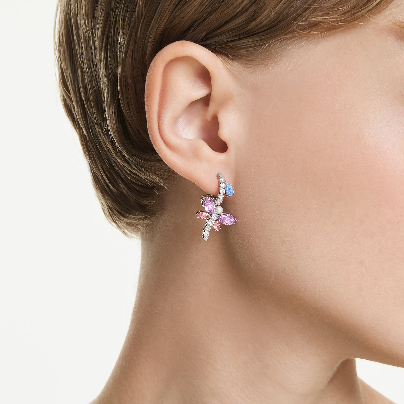 Swarovski Ohrring aus Metall mit rosa, lila und blauen Schmetterlings-Kristallen am Ohr einer Person.