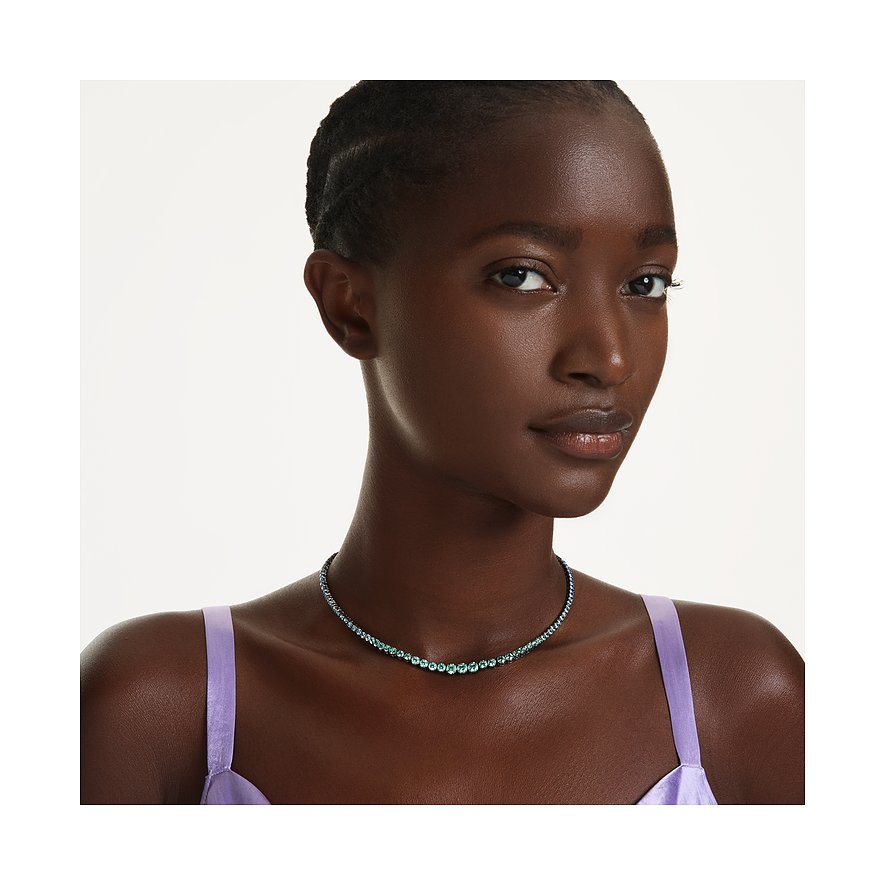 Eine Frau trägt ein Swarovski Metall-Halsschmuck mit grünen Farbsteinen, wobei die mittleren Kristalle größer sind.