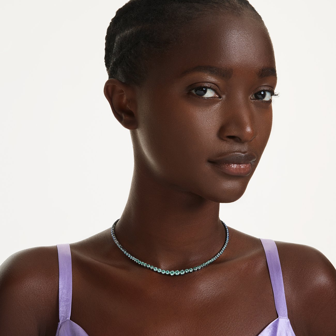 Eine Frau trägt ein Swarovski Metall-Halsschmuck mit grünen Farbsteinen, wobei die mittleren Kristalle größer sind.