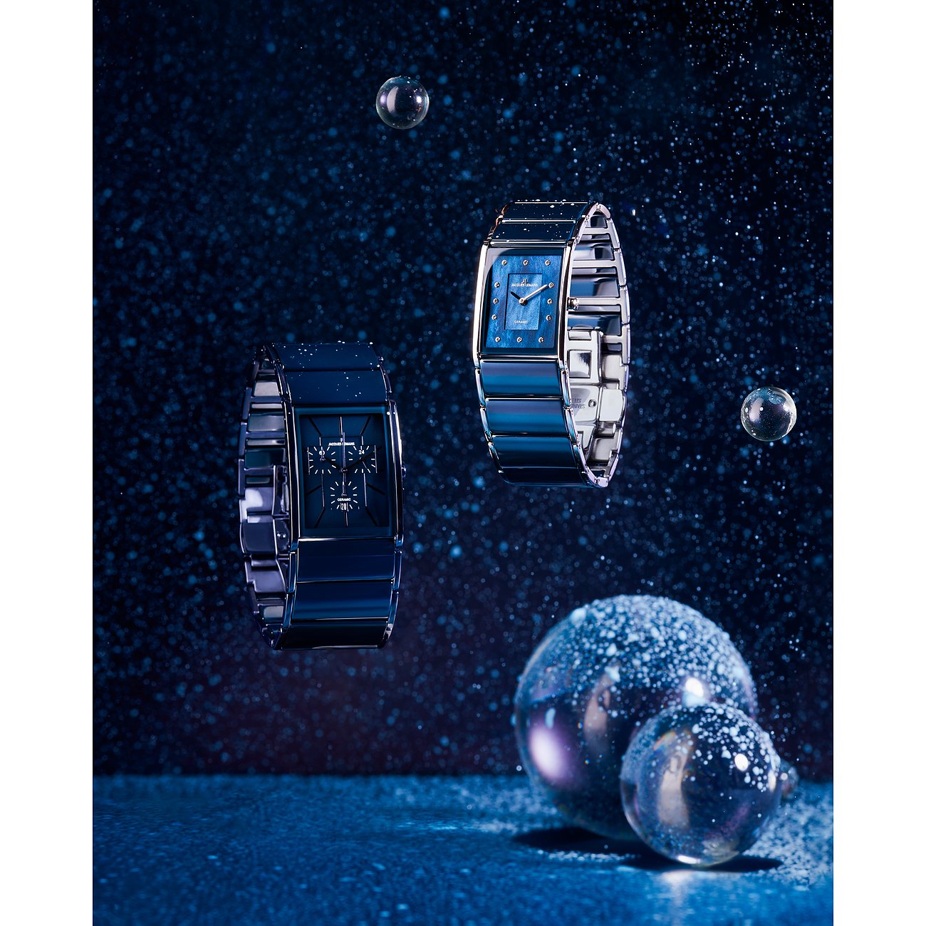 Zwei schwebende Jacques Lemans Damenuhren aus blau gefärbtem Edelstahl vor dunklem Hintergrund mit glitzernden Details.