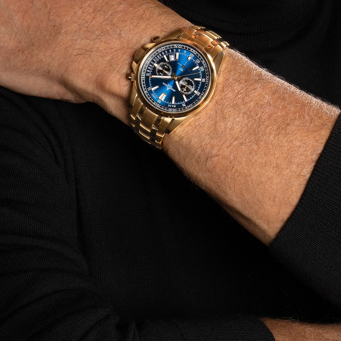 Jacques Lemans Herrenuhr aus blauem und goldenem Edelstahl am Handgelenk eines Mannes mit schwarzem Rollkragenpullover.