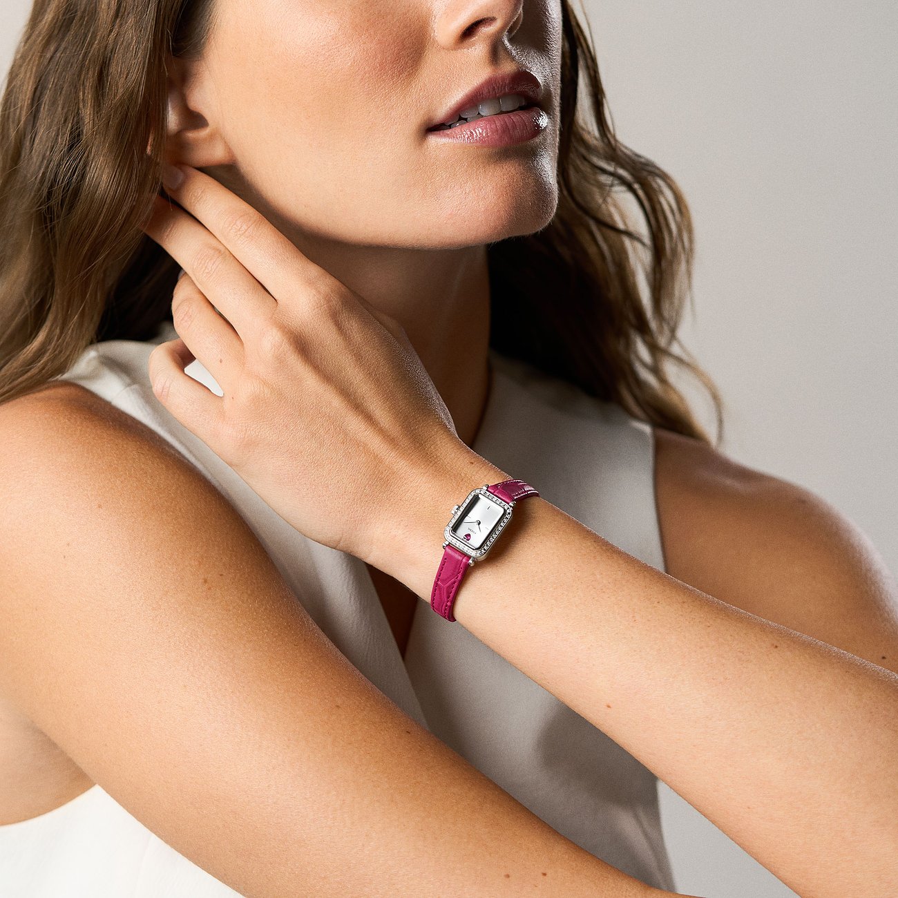 Eine Frau trägt eine rechteckige Fossil Damenuhr aus Edelstahl mit glänzendem Band und einem fuchsiafarbenen Armband.
