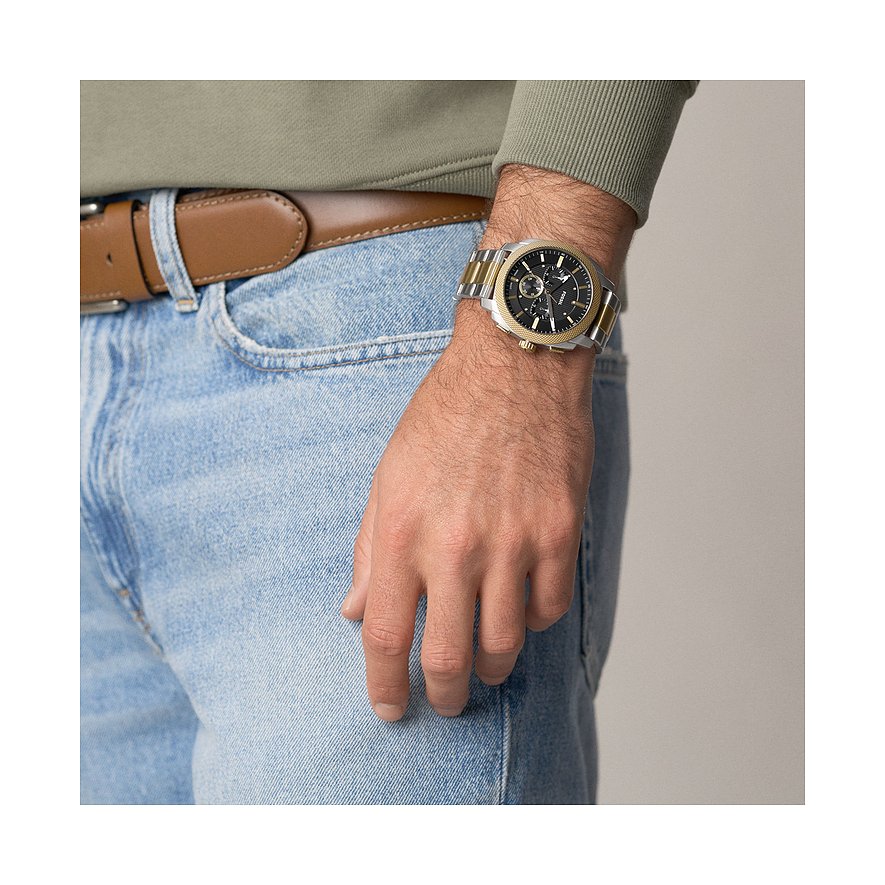 Fossil Herrenuhr aus Edelstahl in Silber und Gold mit schwarzem Zifferblatt am Handgelenk eines Mannes.