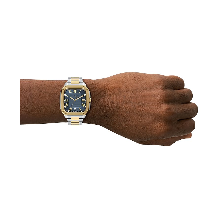 Die Fossil Herrenuhr aus blauem und goldfarbenem Edelstahl befindet sich am Handgelenk einer Person.