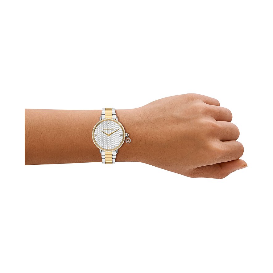 En Michael Kors damklocka i rostfritt stål på handleden, med tvåfärgat guld- och silverfärgat armband.