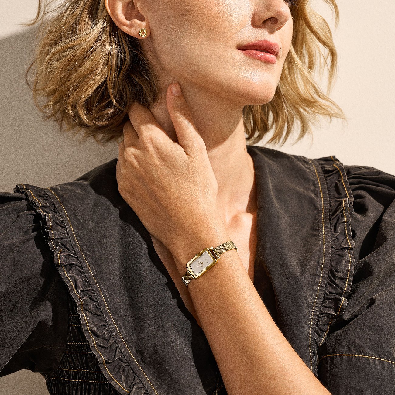 Närbild på kvinna med en rektangulär Skagen-klocka i guldfärgat rostfritt stål. Setet är elegant.