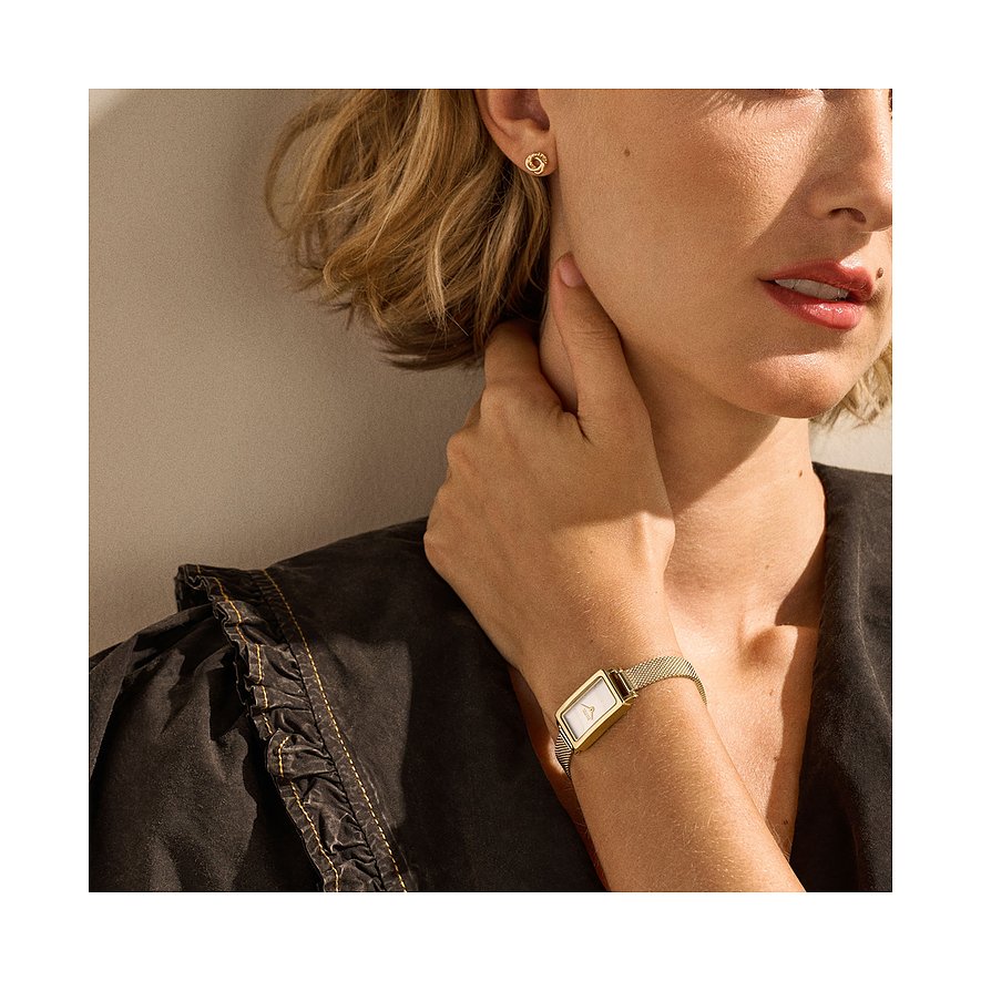 Närbild: Person bär Skagen klockset i guldfärgat rostfritt stål och matchande örhängeskombination.