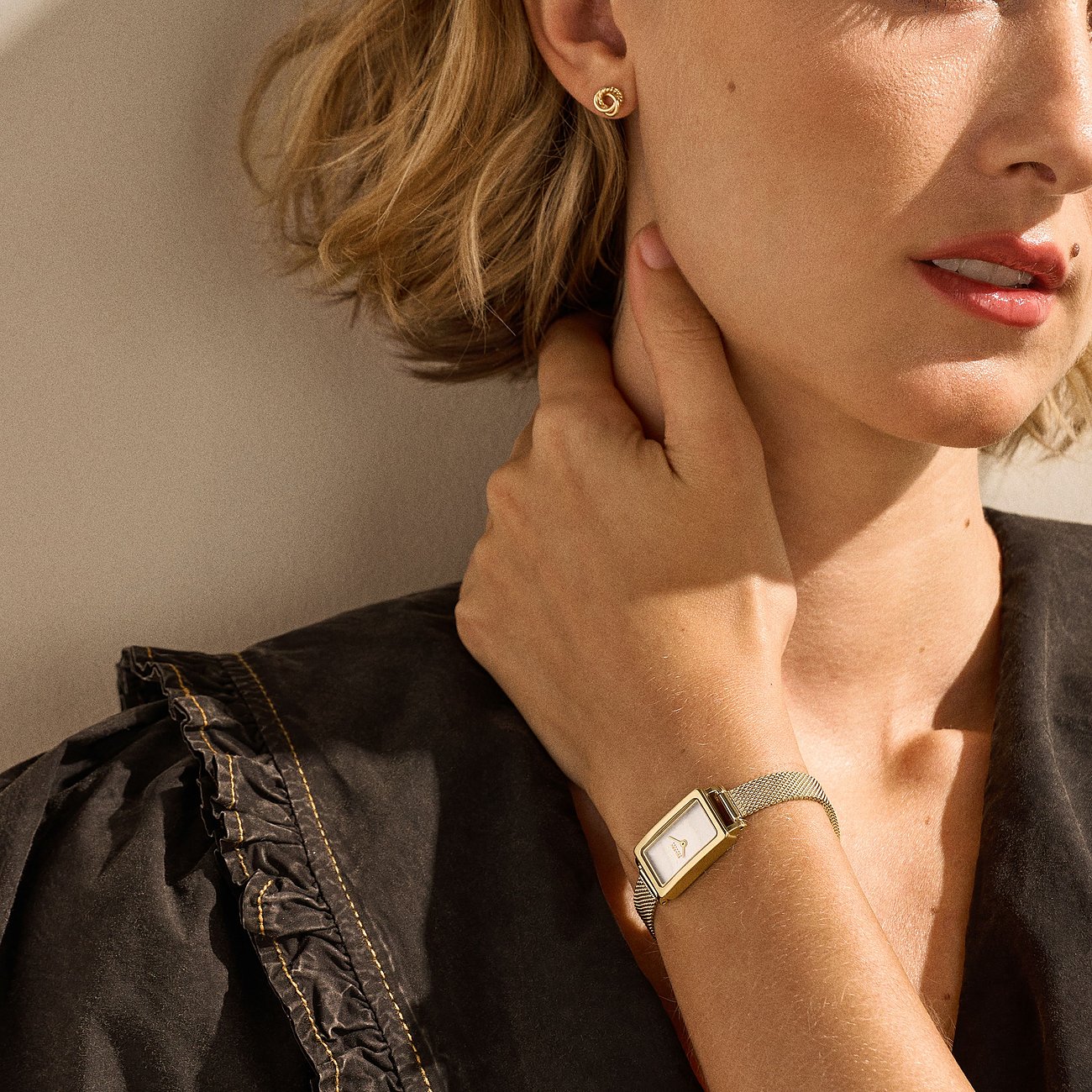 Närbild: Person bär Skagen klockset i guldfärgat rostfritt stål och matchande örhängeskombination.
