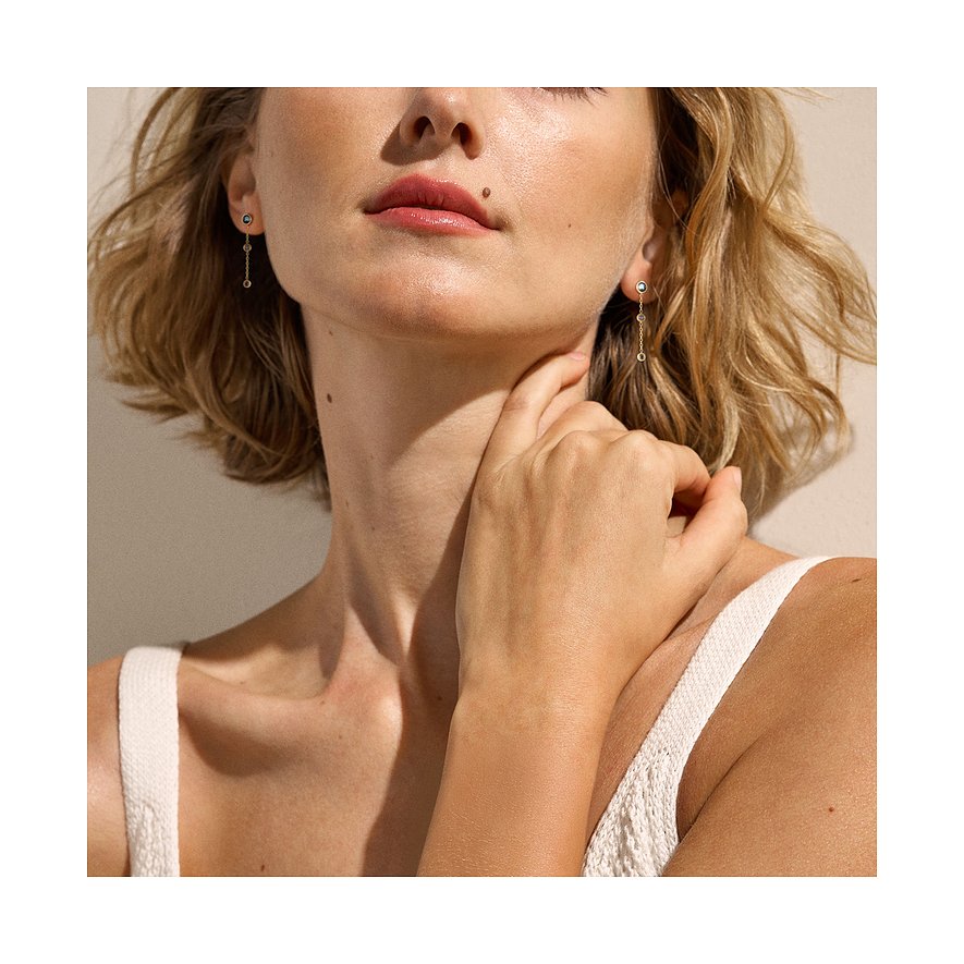 Model trägt Skagen Ohrringe aus Edelstahl mit hängenden Glassteinen an rechtem und linkem Ohr. Die Hand berührt den Hals.