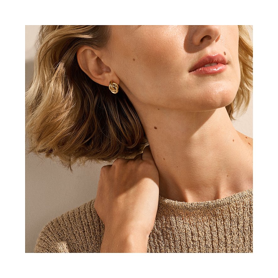 Skagen öronsmycke i rostfritt stål med guldfärgad knutdesign, syns på en kvinnas öra.