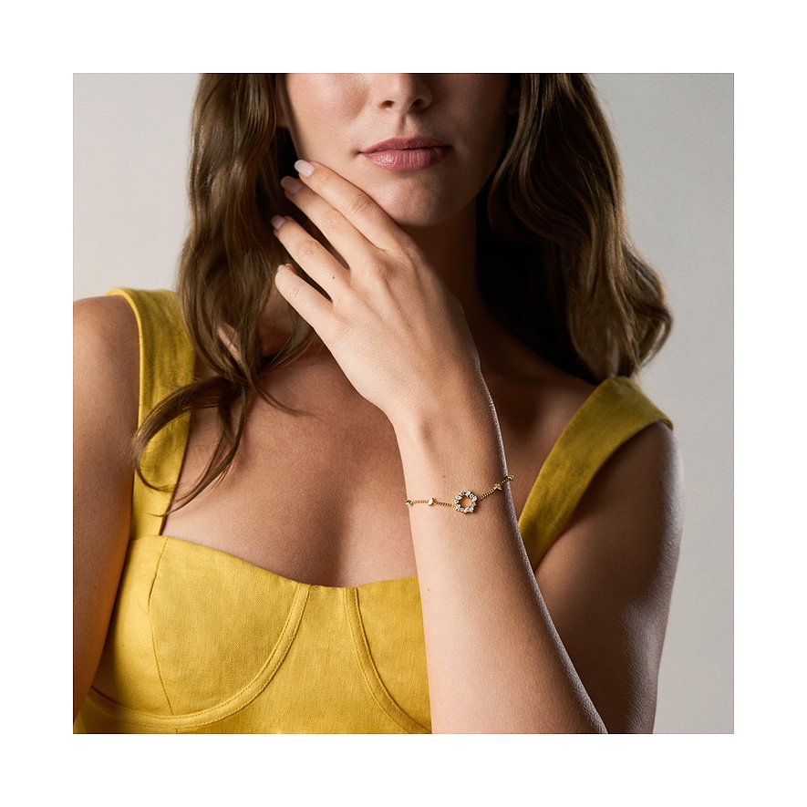 Närbild av ett guld Fossil-armband med blomhänge, prytt med gnistrande glasstenar på vänster hand.