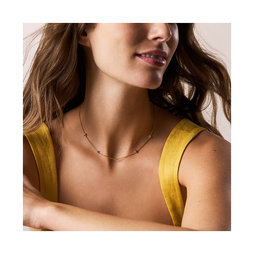 Une femme porte un collier en métal doré Fossil orné de petites pierres circulaires en verre également espacées.