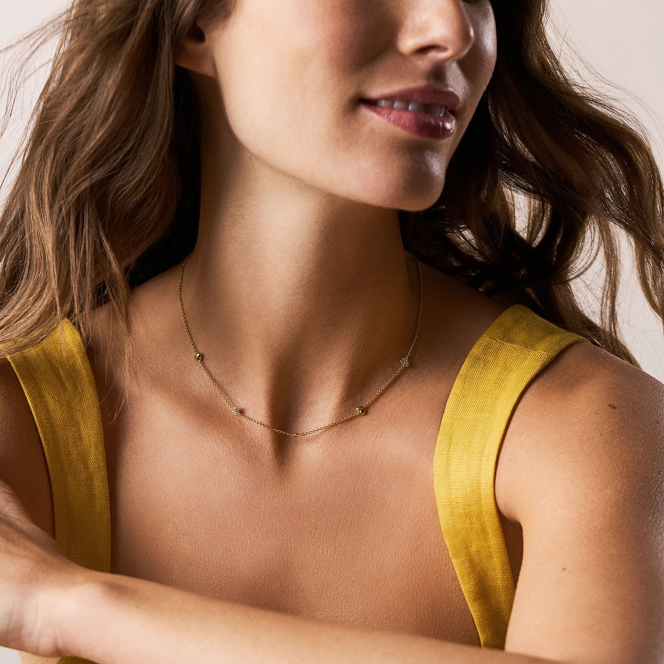 Une femme porte un collier en métal doré Fossil orné de petites pierres circulaires en verre également espacées.