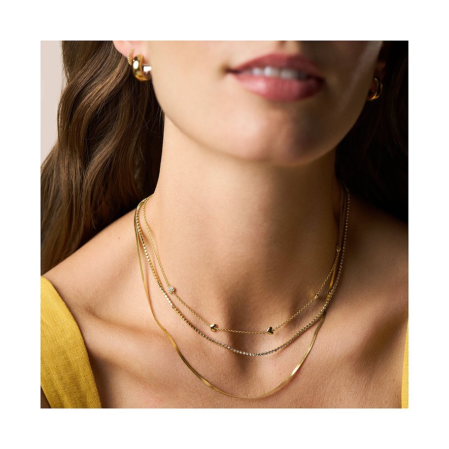 Gros plan d'une femme portant un triple collier Fossil pour femme en métal doré avec pierres en verre clair.