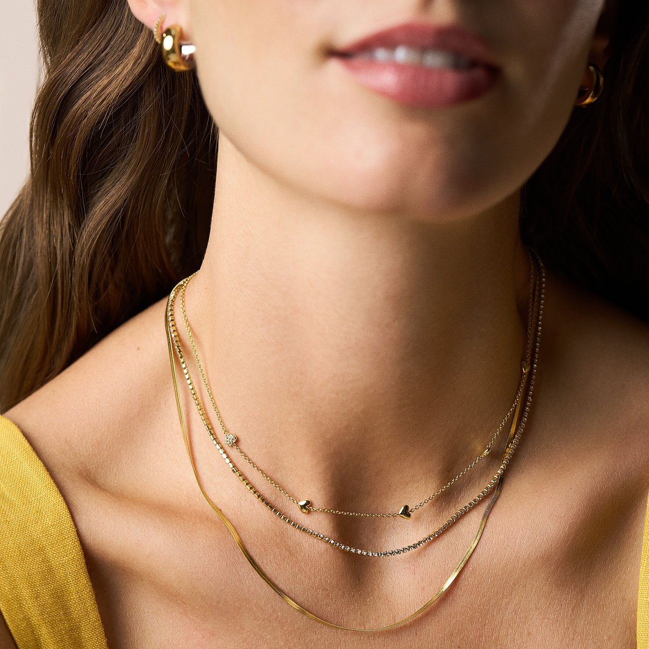 Gros plan d'une femme portant un triple collier Fossil pour femme en métal doré avec pierres en verre clair.