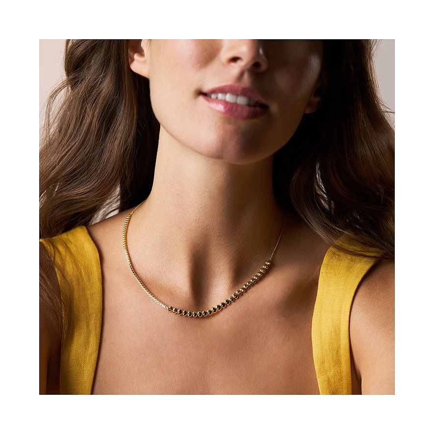 Close-up van een vrouw die een Fossil metalen ketting draagt met kleine gouden en zwarte glasstenen.