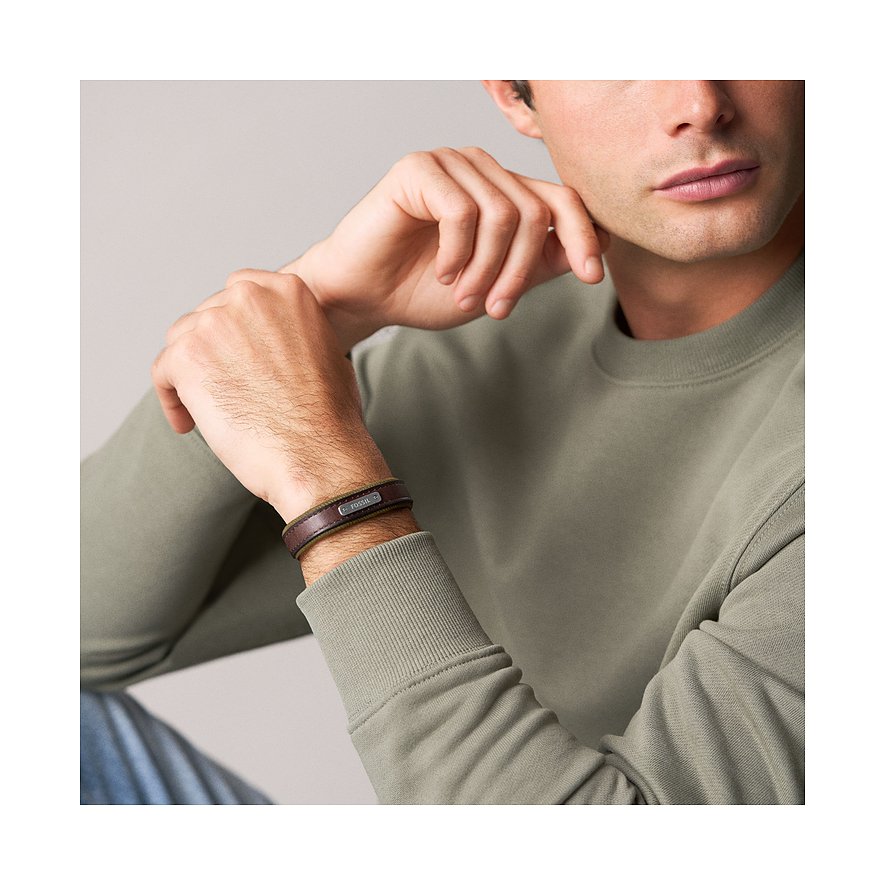 Nahaufnahme eines Mannes, der ein schwarzes Fossil Lederarmband mit kleiner rechteckiger Metallplatte am Handgelenk trägt.