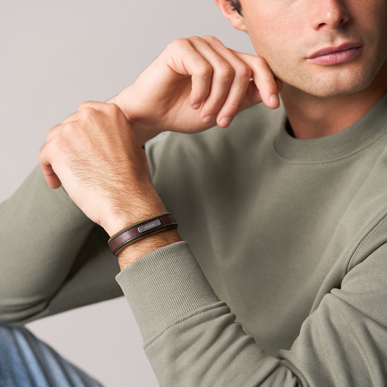 Nahaufnahme eines Mannes, der ein schwarzes Fossil Lederarmband mit kleiner rechteckiger Metallplatte am Handgelenk trägt.