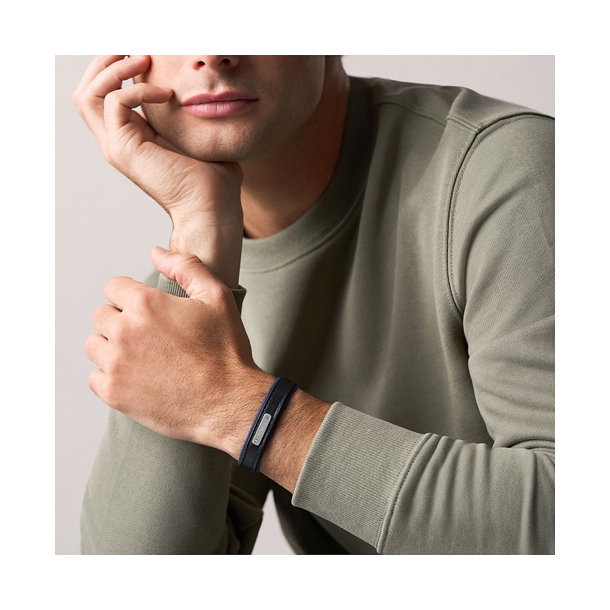 Un uomo in maglione grigio, mano sul mento, indossa un bracciale Fossil in pelle blu e metallo.