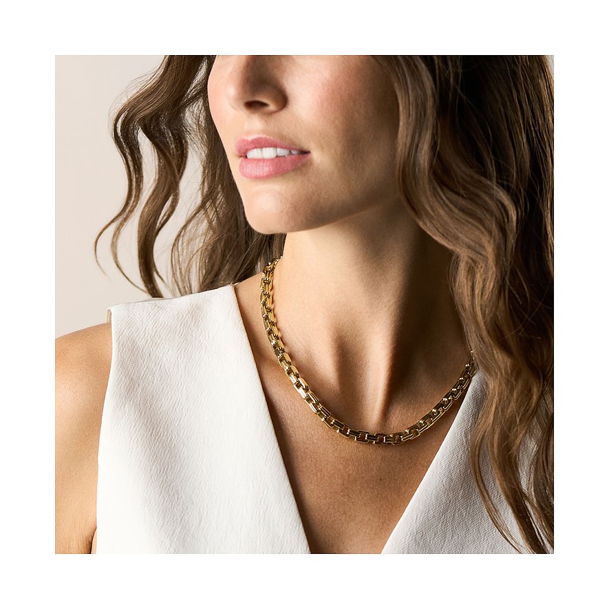 Eine Frau trägt eine goldfarbene Fossil Halskette aus Edelstahl, die elegant ihr Dekolleté ziert.