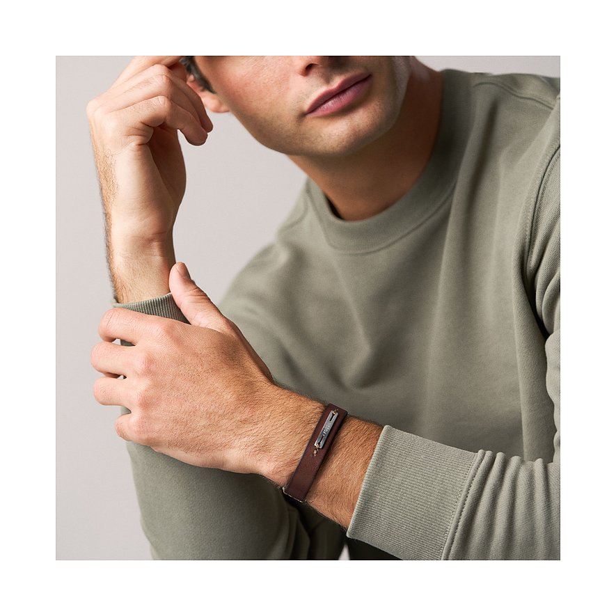 Ein Mann trägt das Fossil Armband. Es ist ein braunes Lederarmband mit einer Edelstahlplatte, auf der „Fossil“ steht.