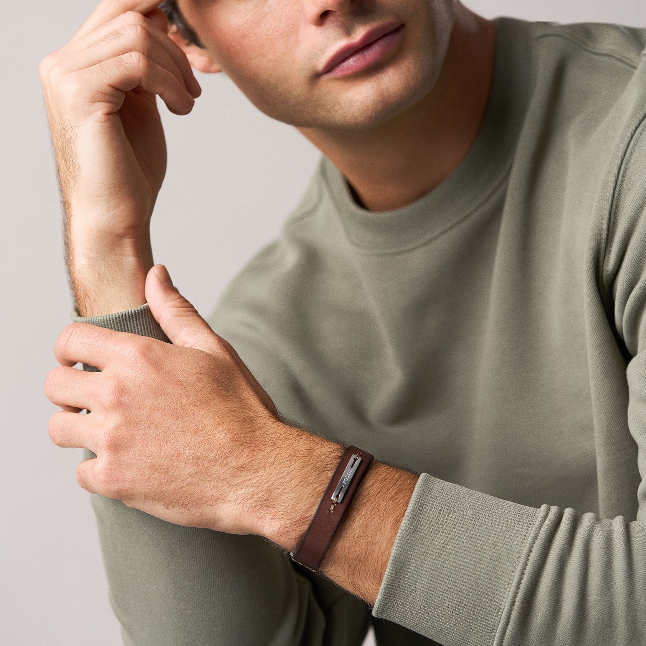 Ein Mann trägt das Fossil Armband. Es ist ein braunes Lederarmband mit einer Edelstahlplatte, auf der „Fossil“ steht.