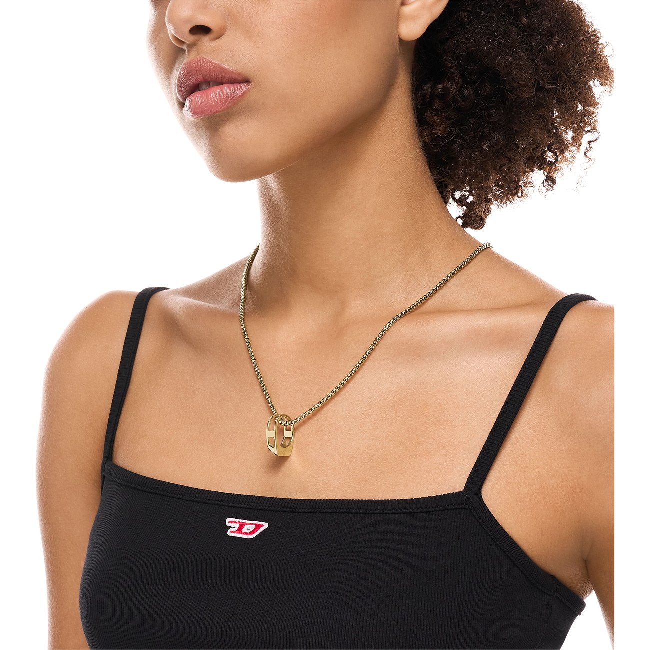En kvinna bär ett guldfärgat Diesel-halsband i rostfritt stål med ett D-format hänge över en svart topp.