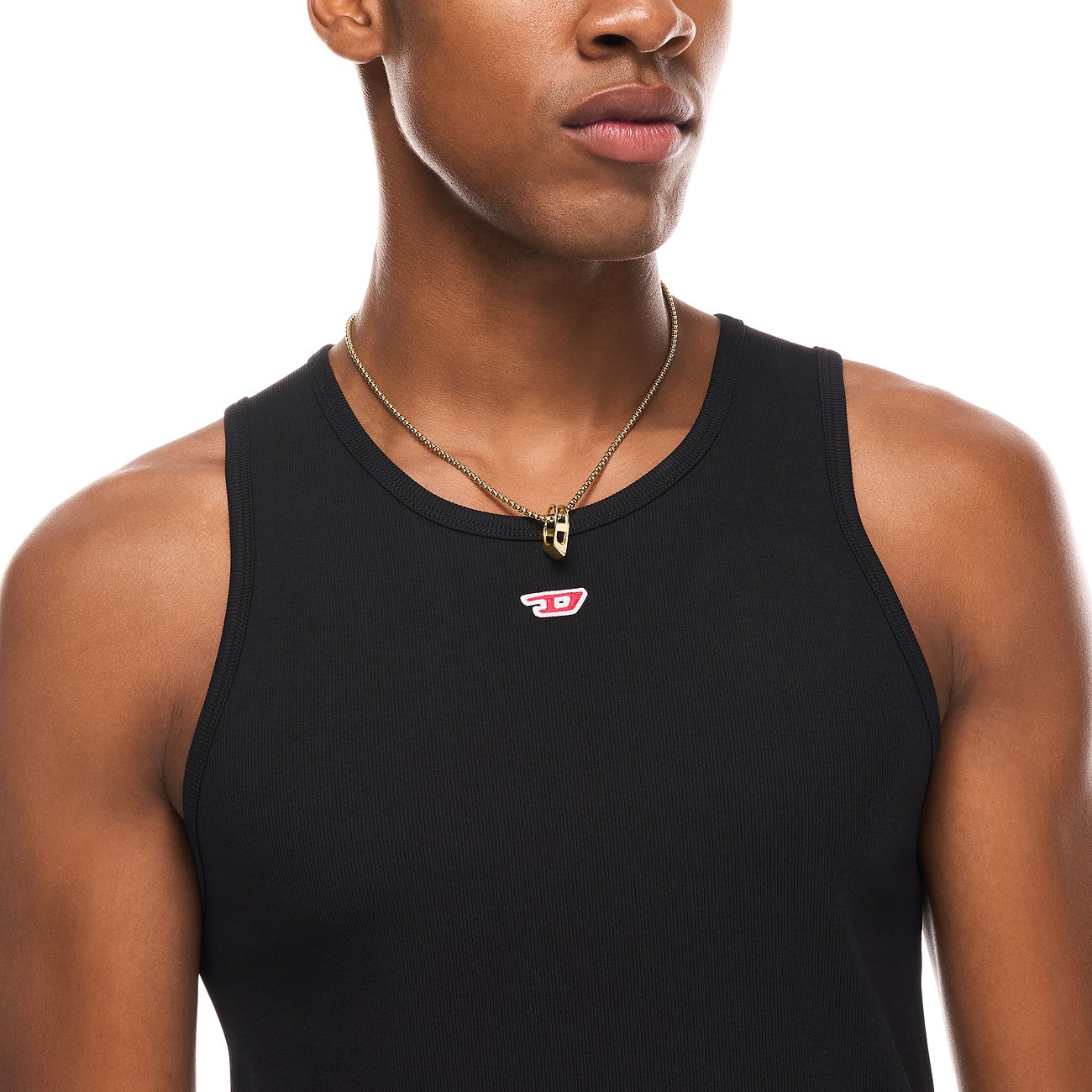 Diesel halsband i guldfärgat rostfritt stål med D-logohänge, buret av en man i svart linne.