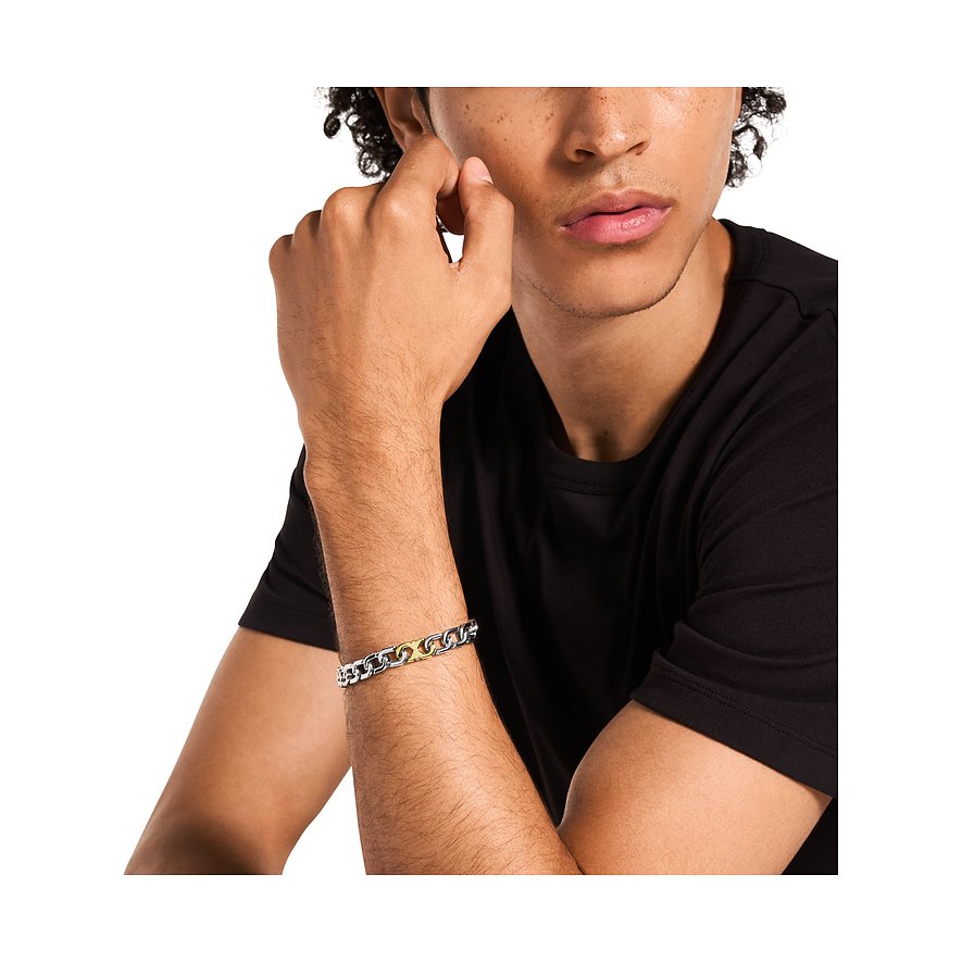 Ein junger Mann trägt ein Emporio Armani Armband aus Edelstahl mit silbernen und goldenen Gliedern.