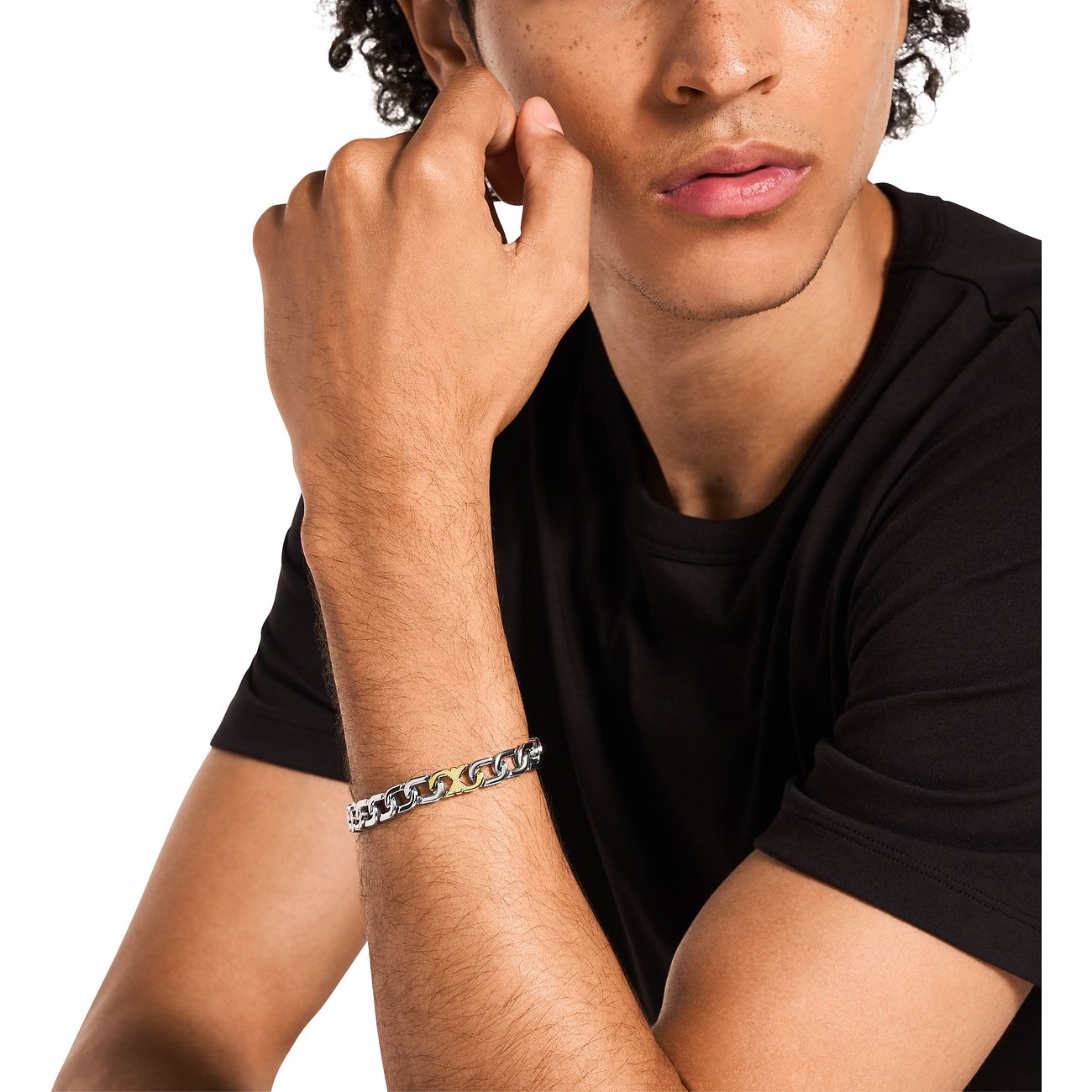 Ein junger Mann trägt ein Emporio Armani Armband aus Edelstahl mit silbernen und goldenen Gliedern.