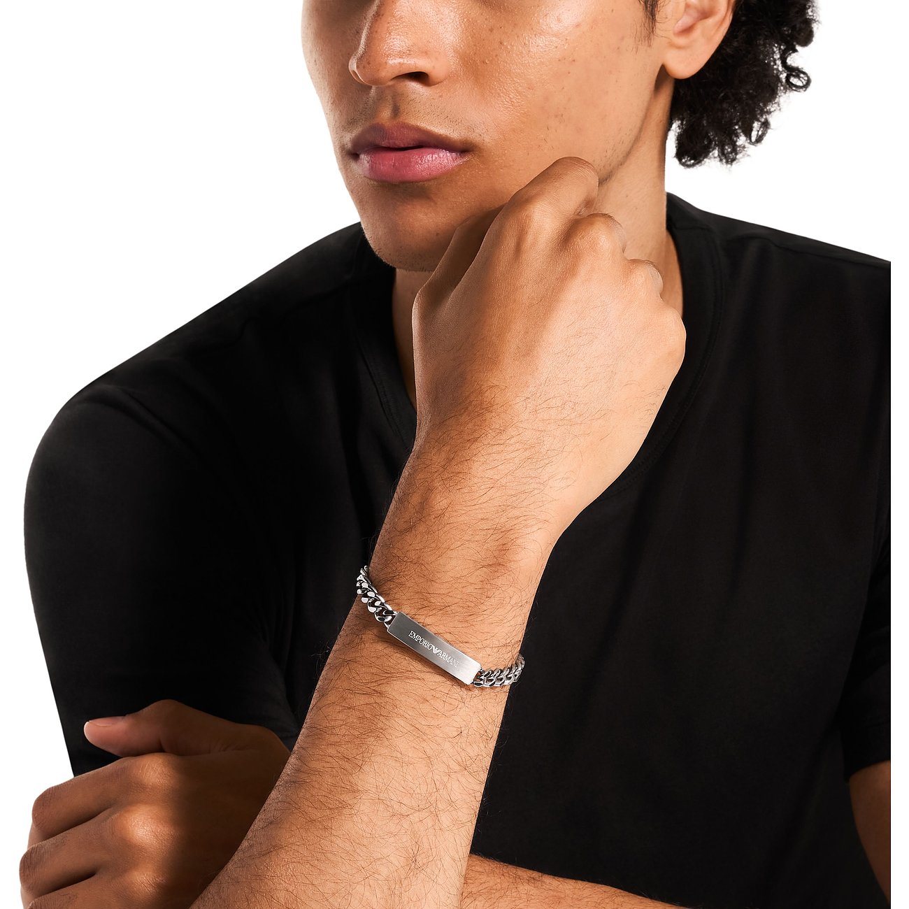 Un uomo indossa un bracciale Emporio Armani in acciaio inossidabile con catena a maglie e barretta incisa.