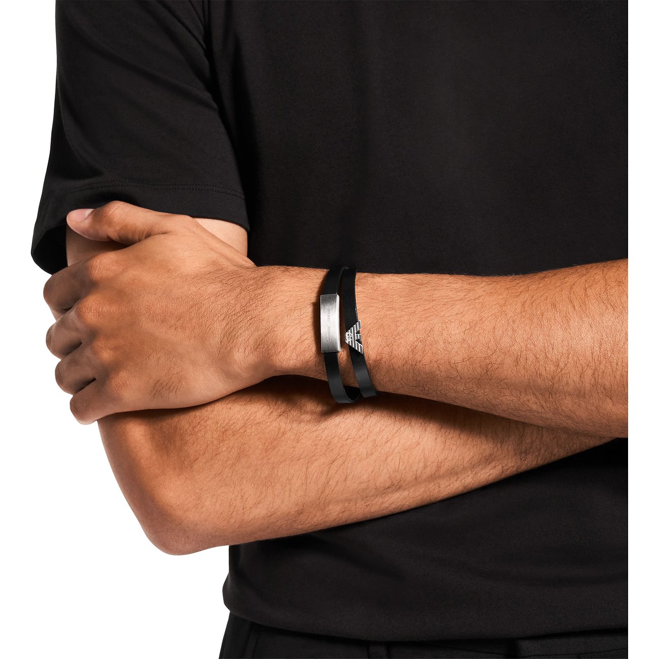 En man bär ett Emporio Armani-armband i svart läder och rostfritt stål, med varumärkets ikoniska örnlogo.