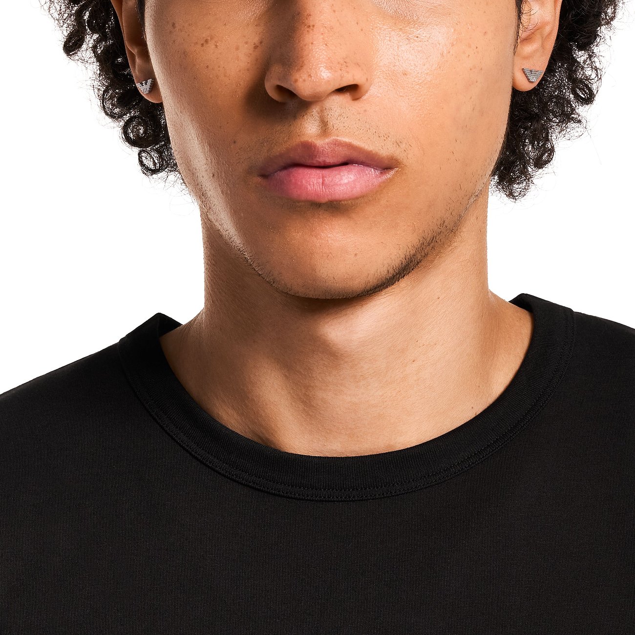 Nahaufnahme eines Mannes, der Emporio Armani Ohrringe aus Edelstahl mit einem Adler-Logo-Motiv trägt.
