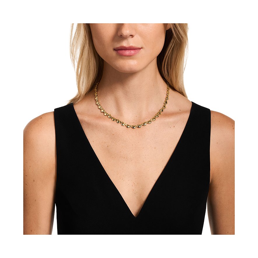 Una donna indossa una collana Emporio Armani in metallo color oro con maglie a cuore attorno al collo.