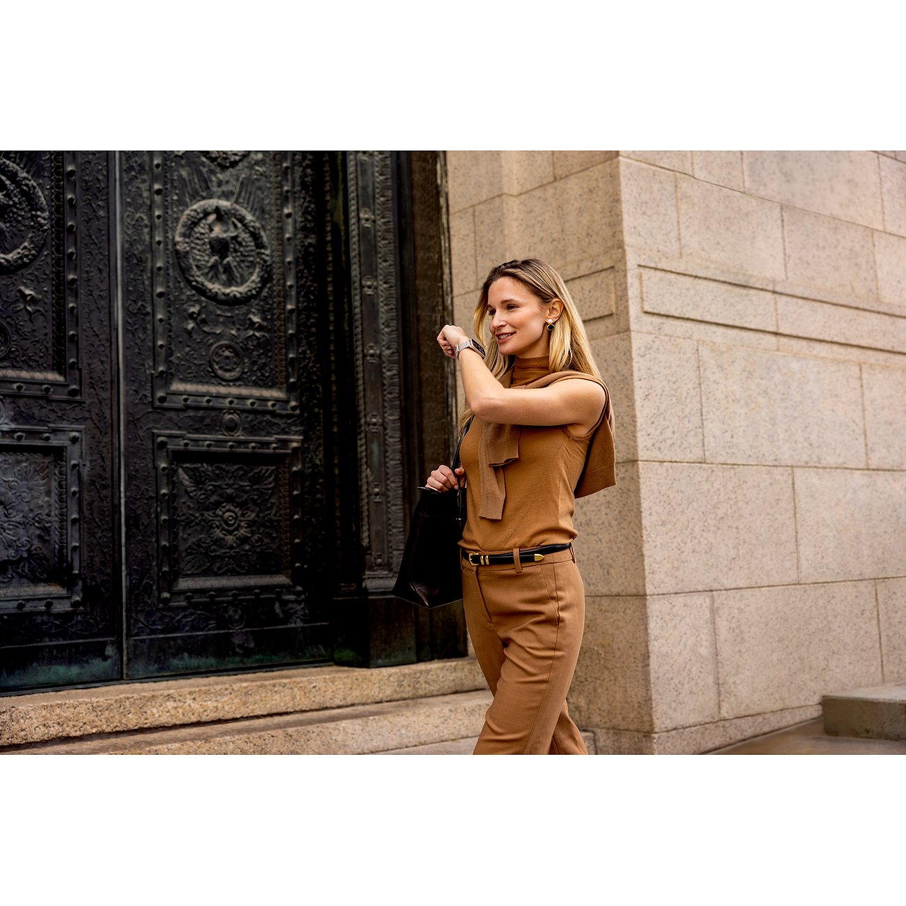 Eine Frau in brauner Kleidung, die eine Garmin Smartwatch aus Kunststoff und Metall am Handgelenk trägt und darauf schaut.