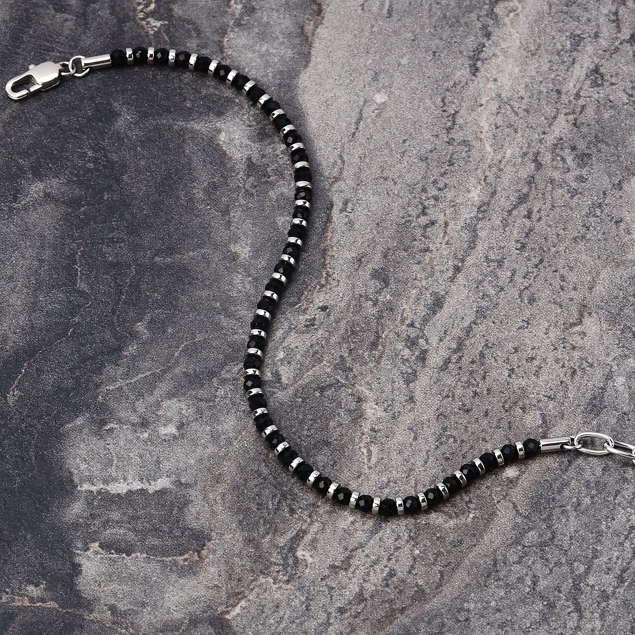 Ett detaljerat Morellato armband i rostfritt stål med svarta agatfärgade stenar, liggande på en mörk yta.