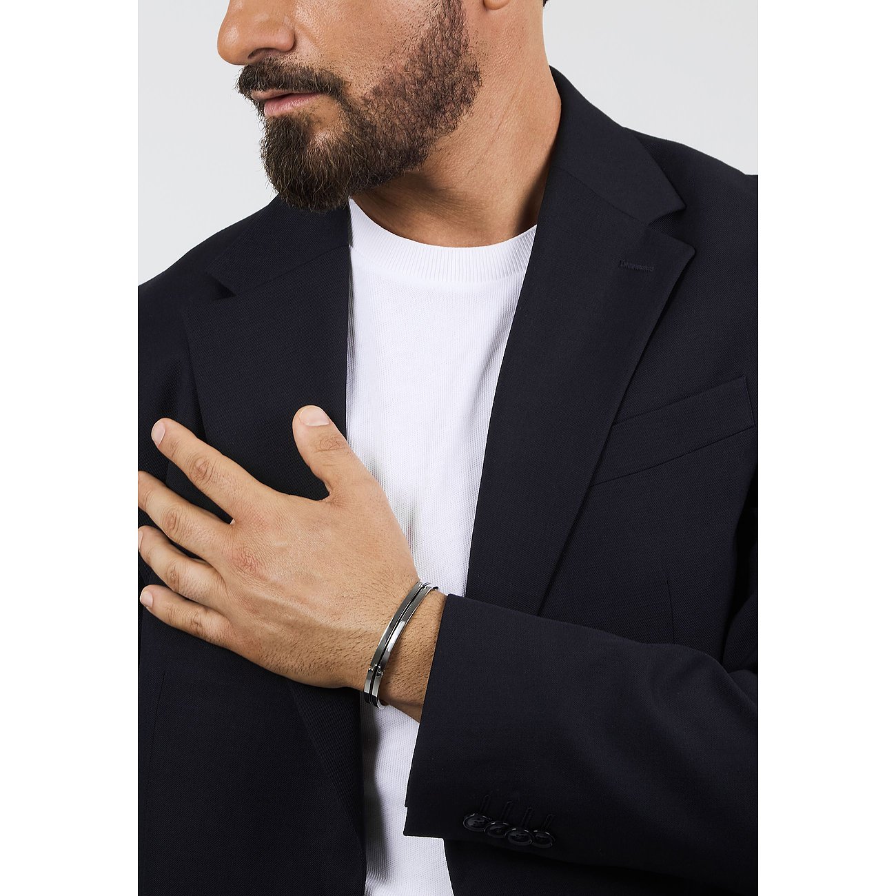 Nahaufnahme eines Mannes im Anzug, dessen Hand auf der Brust liegt und ein Morellato Armschmuck aus Edelstahl trägt.