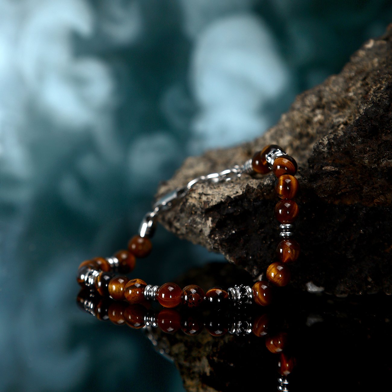 Morellato Edelstahlarmband mit dunkelbraunen Tigerauge-Farbsteinen und silberfarbenen Details auf Felsen, reflektiert.