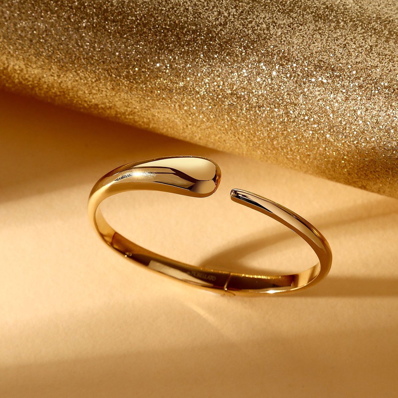 Ein glänzender goldfarbener Morellato Edelstahl-Armreif mit offener Vorderseite, schwebend über glitzerndem Hintergrund.