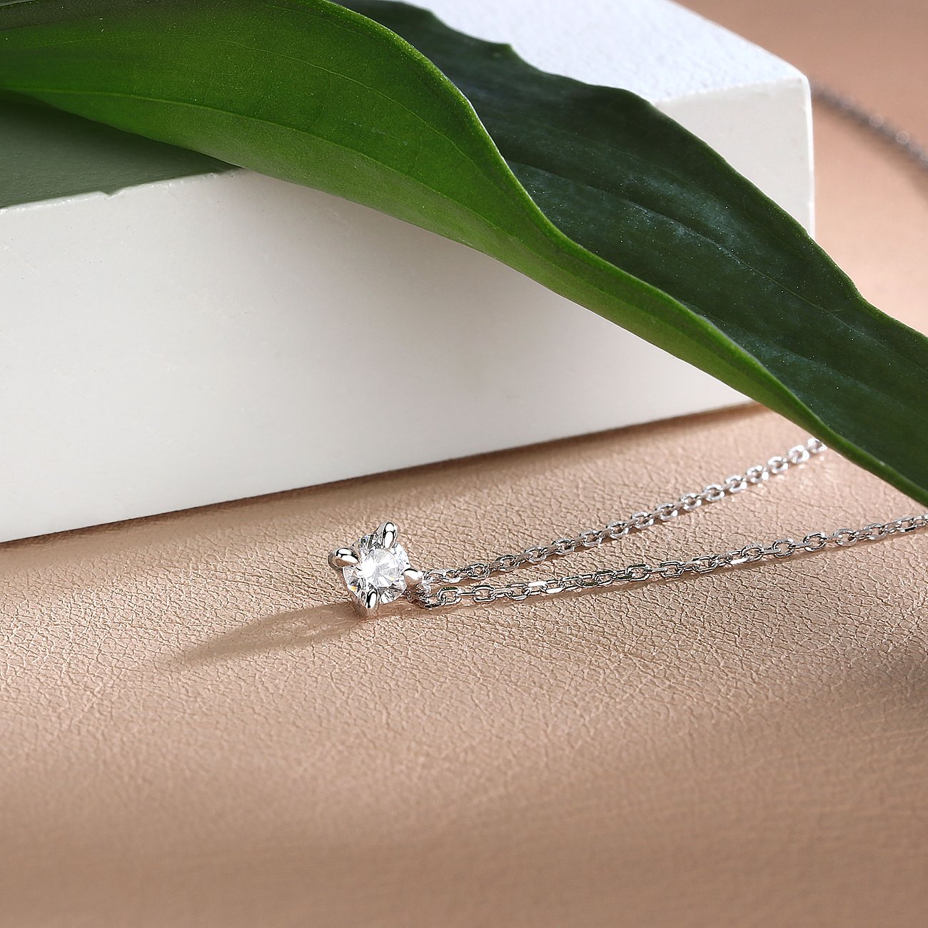 CHRIST Halsschmuck aus glänzendem Gelbgold mit funkelndem runden Diamanten in 4-Krappen-Stein. Grüne Pflanze auf weißem Objekt.