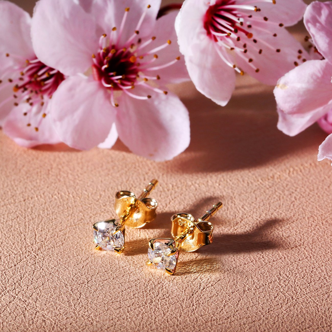 CHRIST oorstekers van 585 geelgoud met fonkelende diamanten als hoofdstenen, gepresenteerd voor roze bloesems.