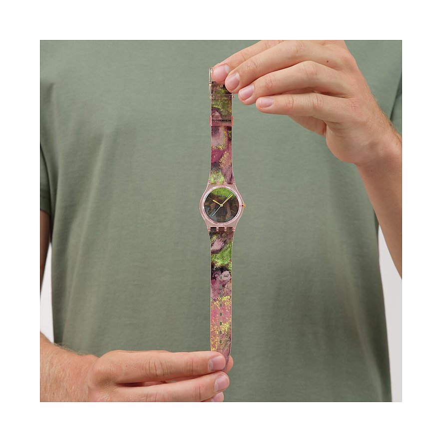 Ein Mann hält eine Swatch Unisexuhr aus Kunststoff mit einem bunten, gemusterten Armband und rosafarbenem Gehäuse.